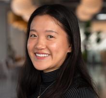 Diane smiles at the camera. She has shoulder-length black hair and wears a black and grey striped shirt