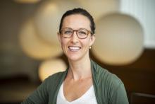 Whitney is centered in frame with a blurred background. She is wearing tortoiseshell glasses, earrings, and white shirt and green cardigan.